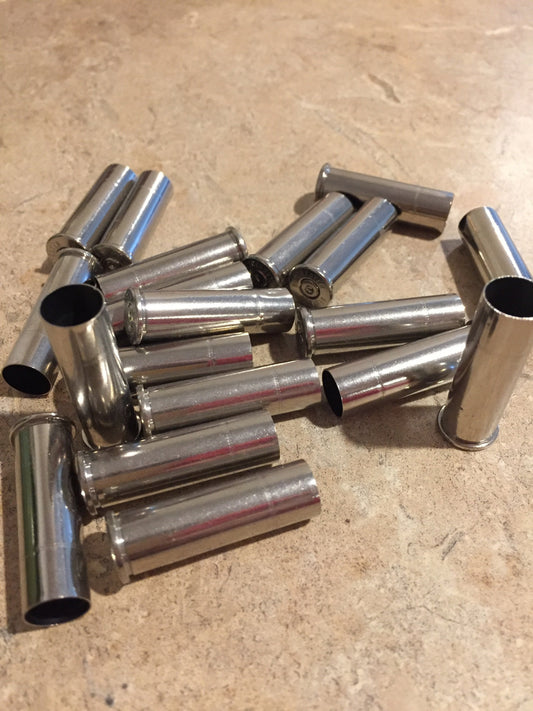 Pile of silver nickel .357 Magnum casings with open mouths scattered on a tan countertop