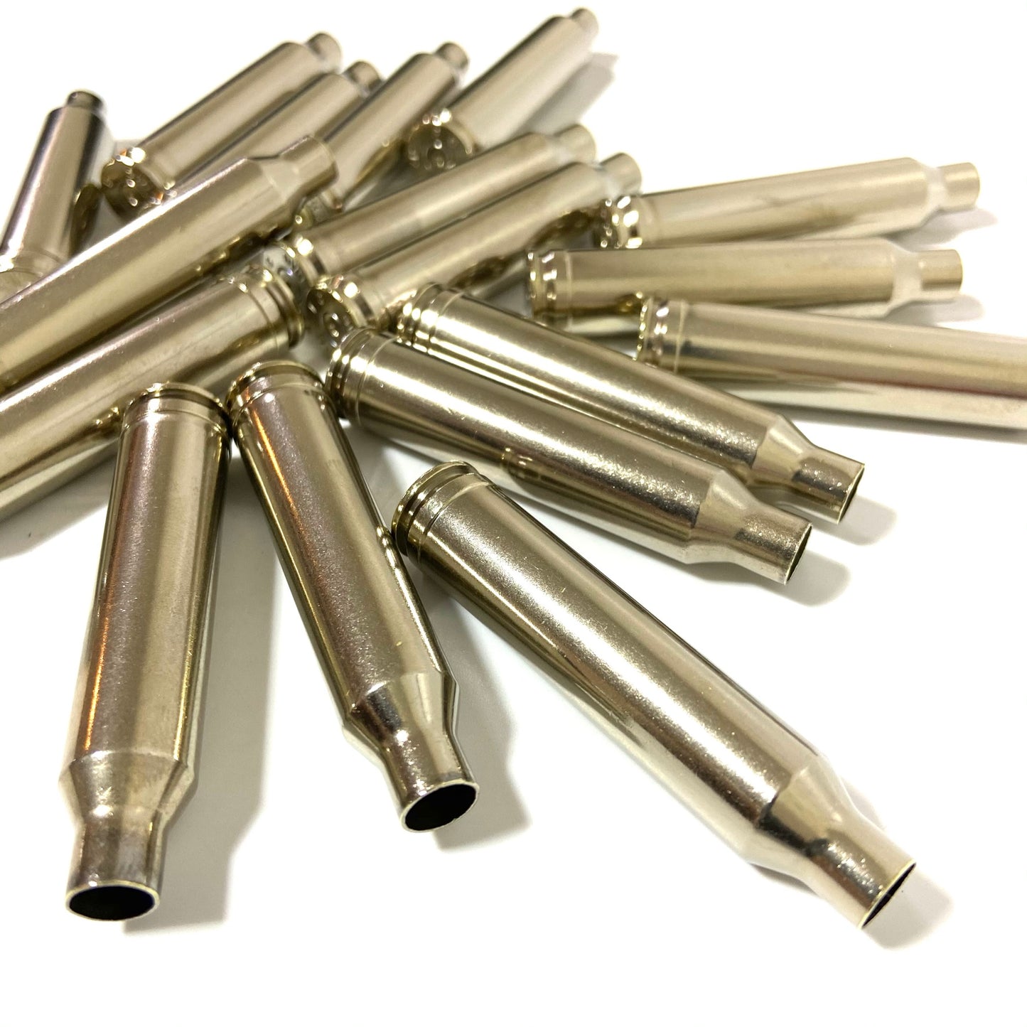 Close-up view of empty polished nickel brass rifle bullet casings scattered on a clean surface.
