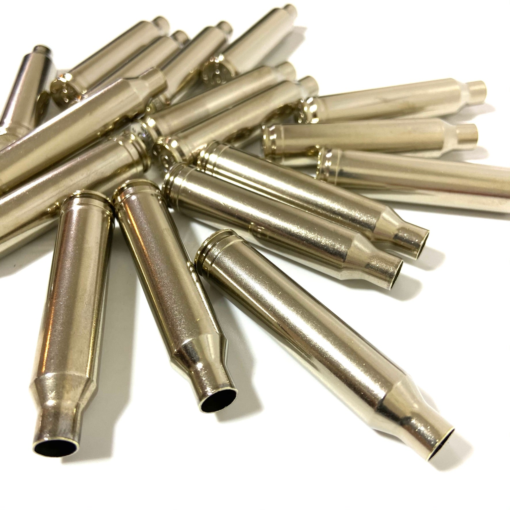 Close-up view of empty polished nickel brass rifle bullet casings scattered on a clean surface.

