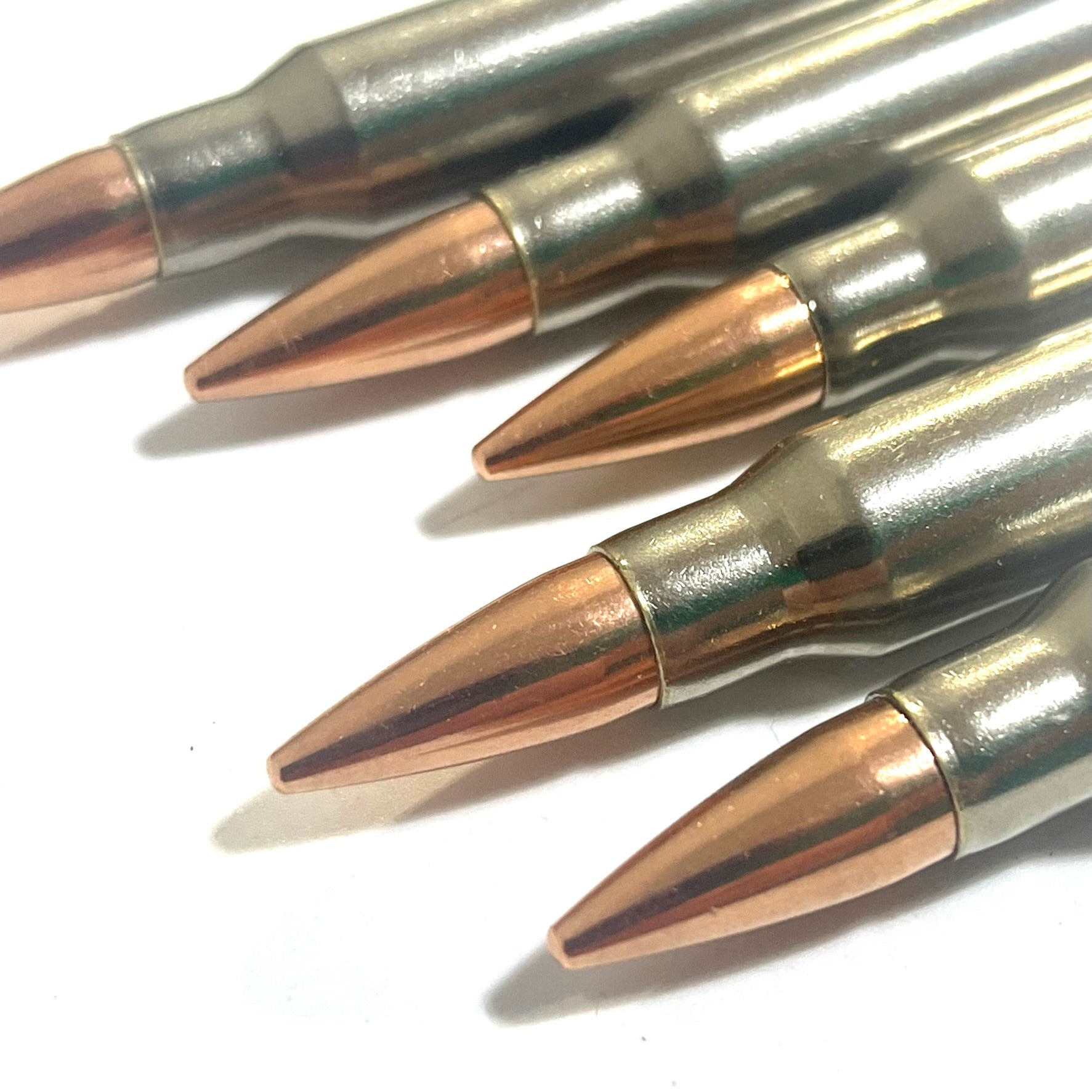 Close-up of five nickel-plated .308/7.62x51 dummy cartridges angled with copper bullet tips facing the camera
