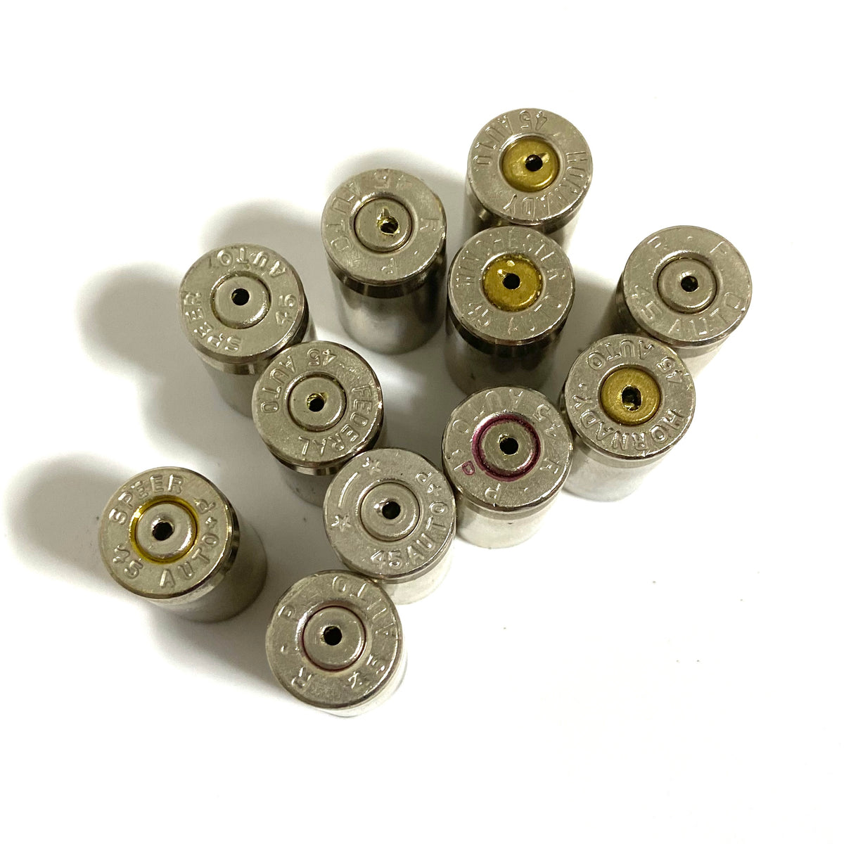 Overhead view of eleven once-fired nickel 45 ACP shells, headstamps up with drilled primers