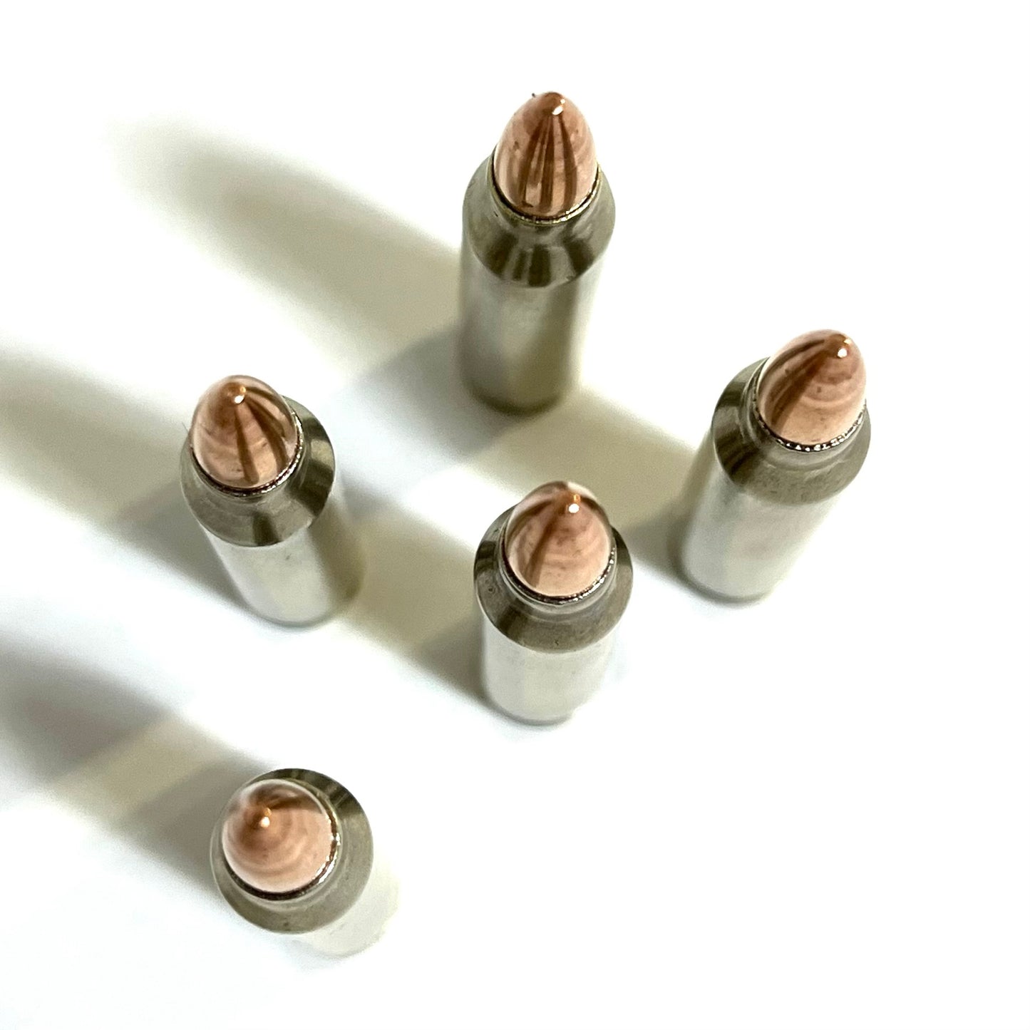Top view of 5 nickel-plated .223 dummy rifle cartridges standing upright showing base rims and copper bullet tips.