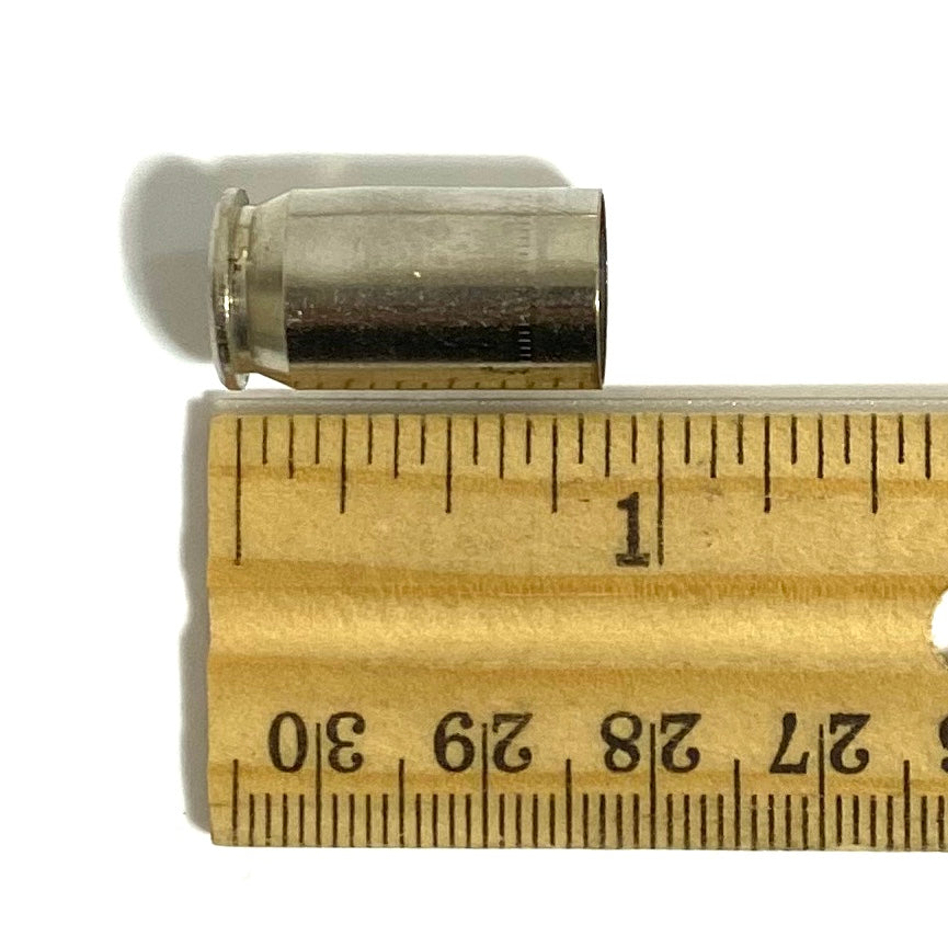 Spent nickel 45 ACP case lying above a wooden ruler, measuring just under 1 inch long