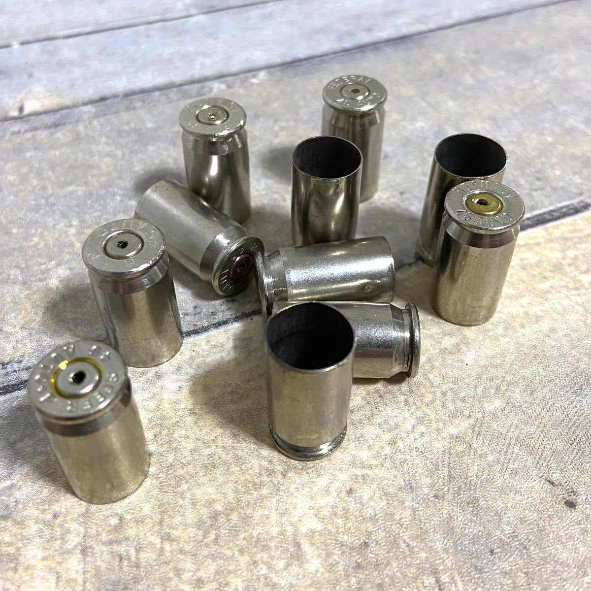 Used nickel 45 ACP shells standing and lying on a weathered wood plank floor, headstamps facing up