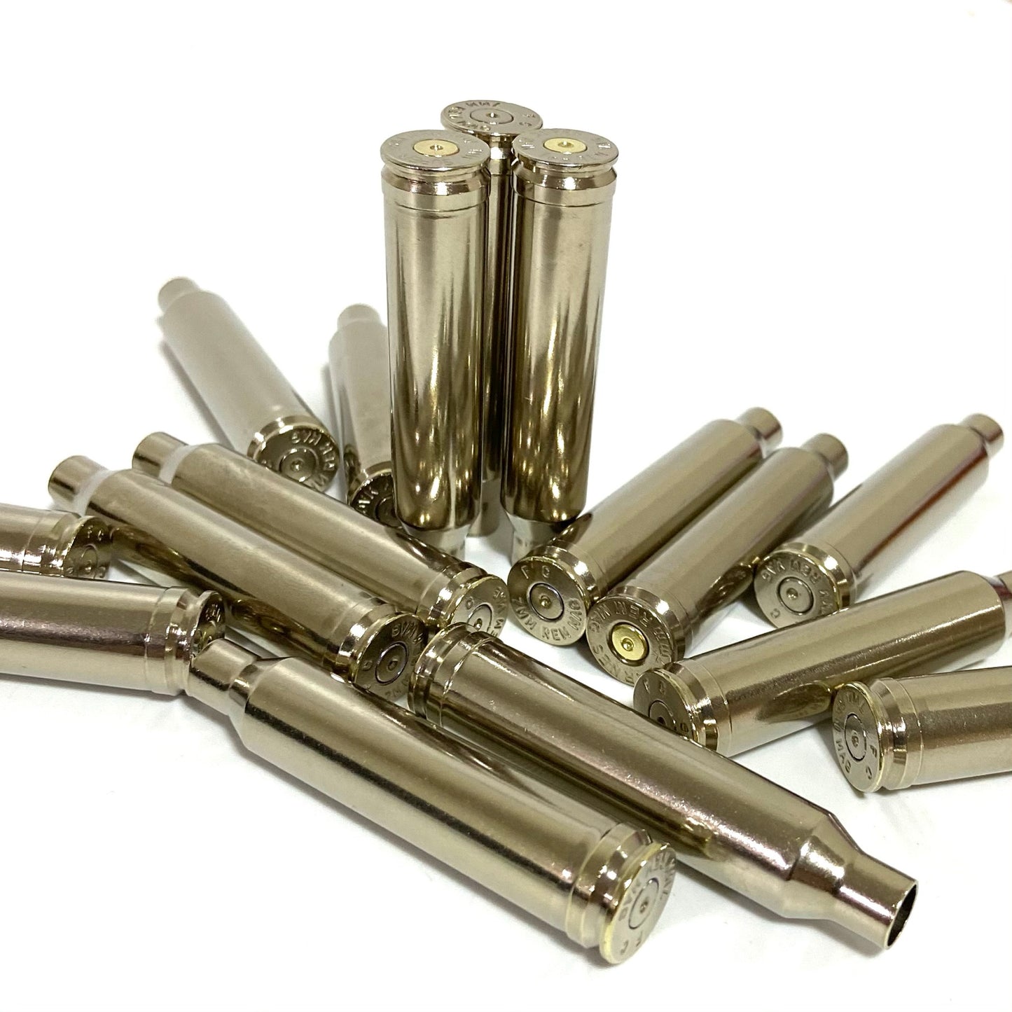 A pile of empty once-fired nickel-plated 7mm Remington Magnum rifle bullet casings on a white background.
