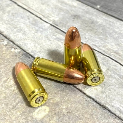 Three 9mm dummy rounds with polished once-fired brass casings and real round-nose bullets on textured surface.
