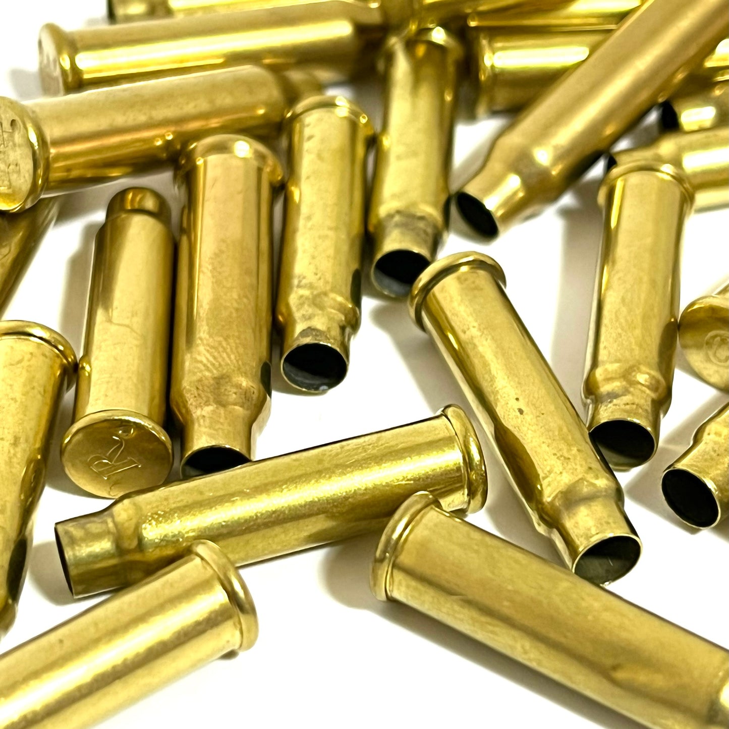 A close-up view of once-fired brass shells showing hollow openings and one base with an R headstamp on a white background.