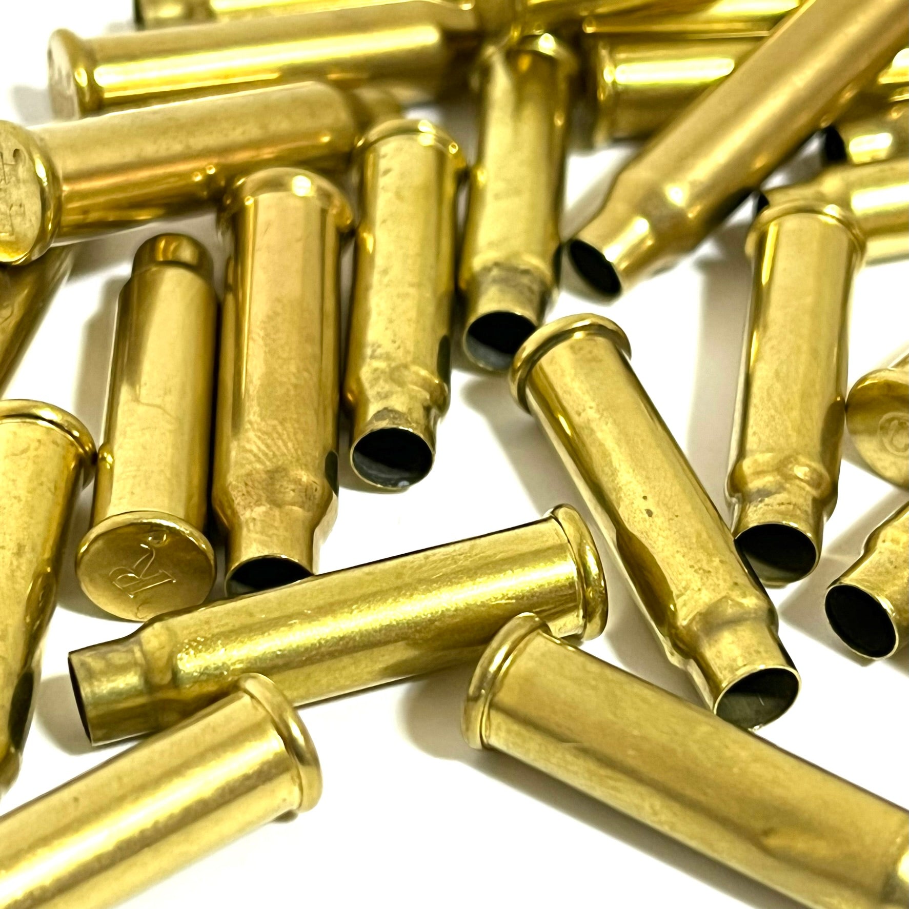 A close-up view of once-fired brass shells showing hollow openings and one base with an R headstamp on a white background.
