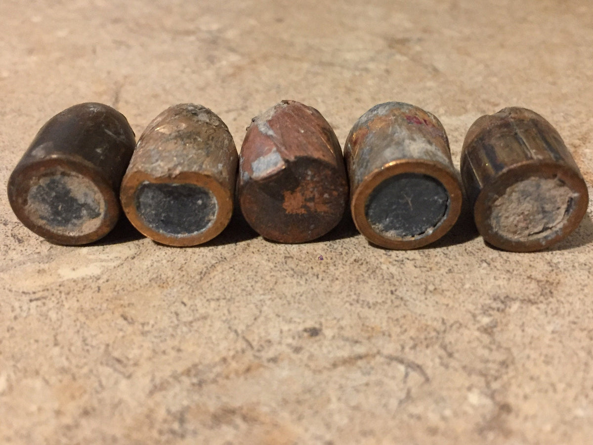 5 spent bullets lying base-out in a row showing flattened lead cores on a stone surface