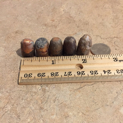 5 tarnished spent bullets standing upright on a stone surface