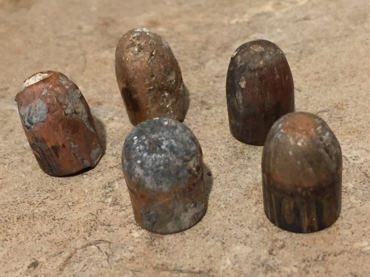 5 tarnished spent bullets standing upright on a stone surface