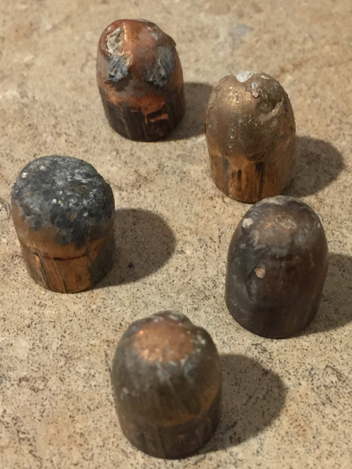 5 tarnished spent bullets standing upright in a cluster on a stone surface