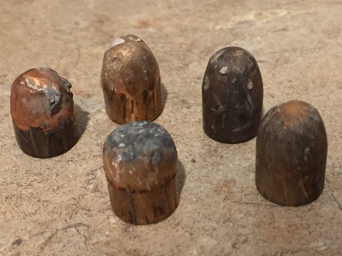 5 tarnished spent bullets standing upright in a cluster on a stone surface