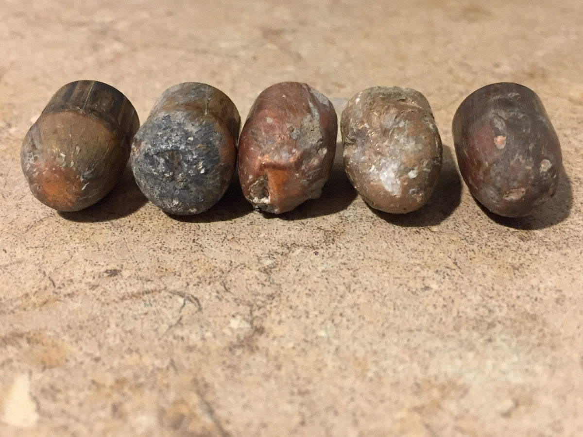 5 tarnished spent bullets lying on their sides on a stone surface