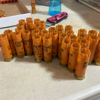 Rows of empty orange Fiocchi Dove Load shotgun shells with gold bases on a table