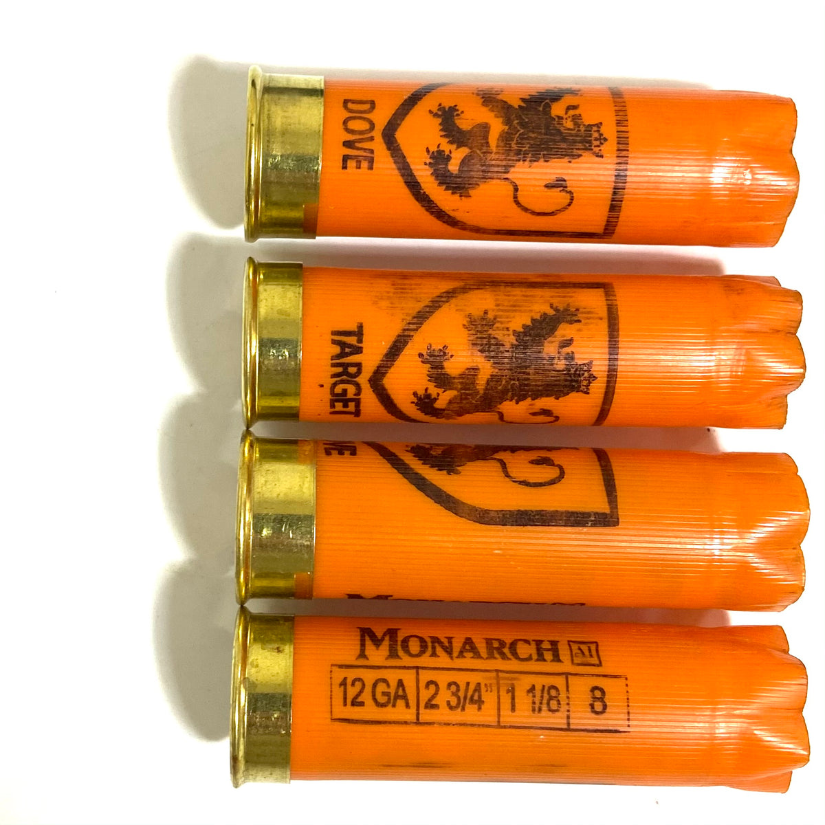 Four orange Monarch 12 gauge shotgun shells with gold bases showing lion crest and Dove printing on hulls