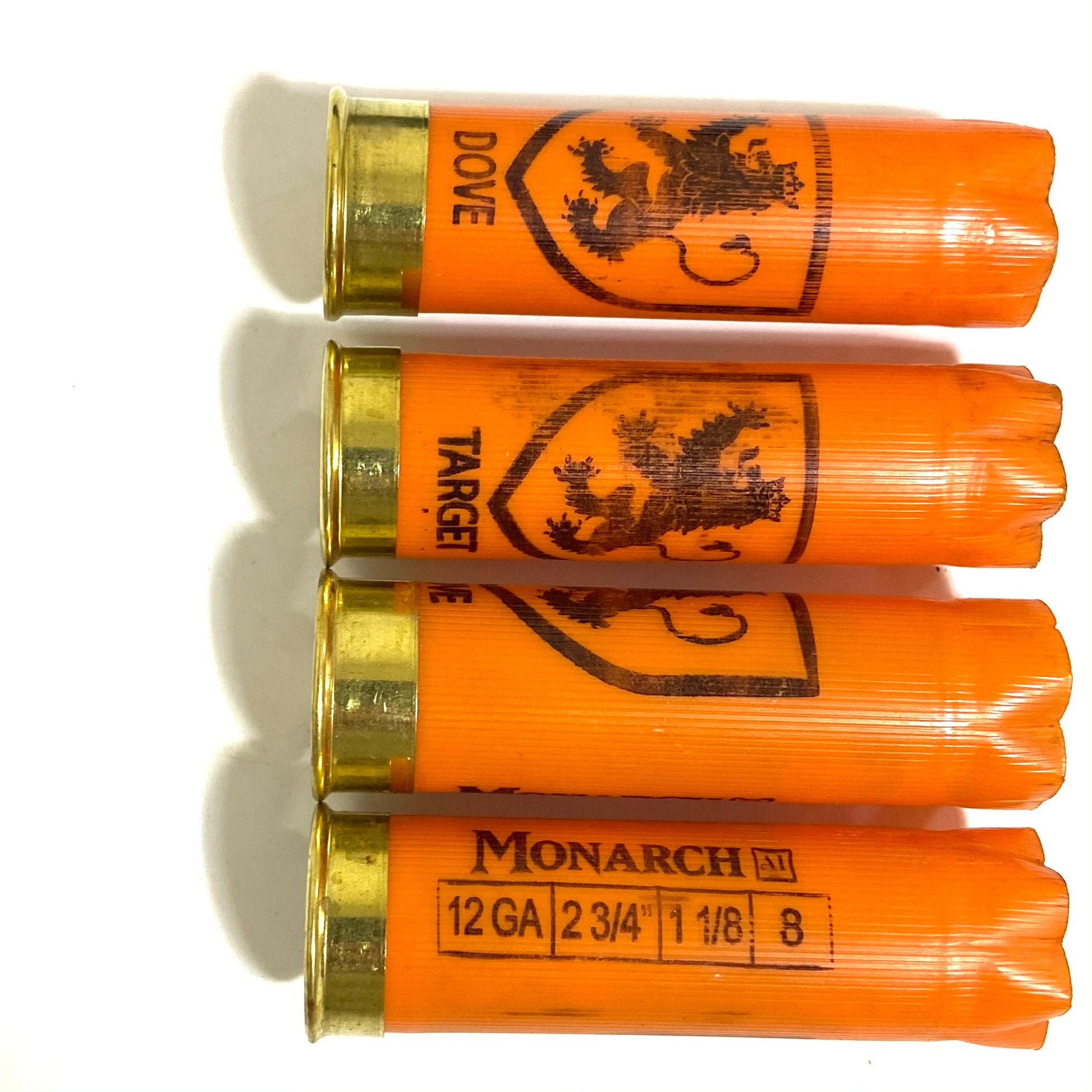 Four orange Monarch 12 gauge shotgun shells with gold bases showing lion crest and Dove printing on hulls