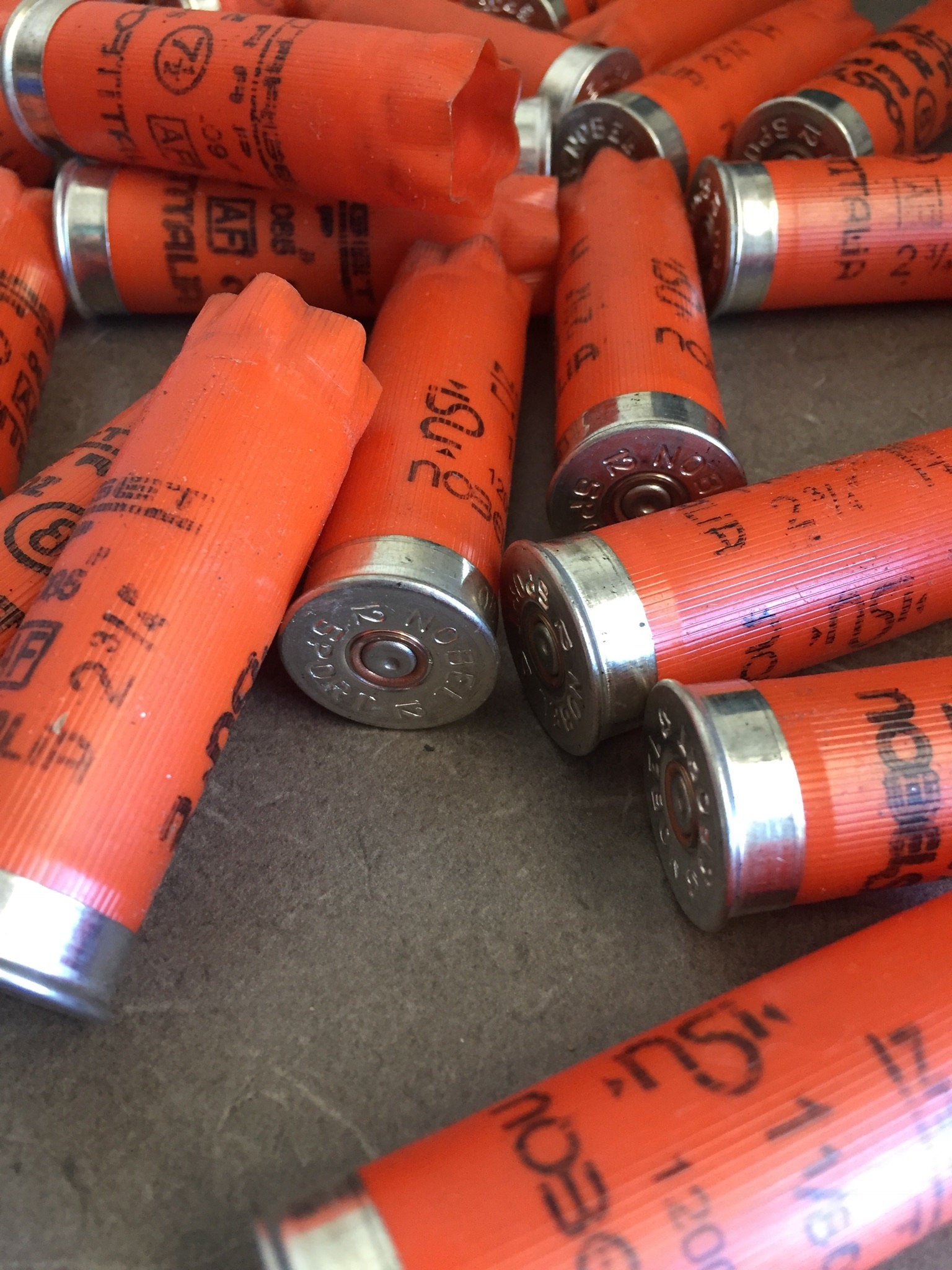 Close-up pile of orange Nobel 12 gauge shotgun shells with silver bases and printed text