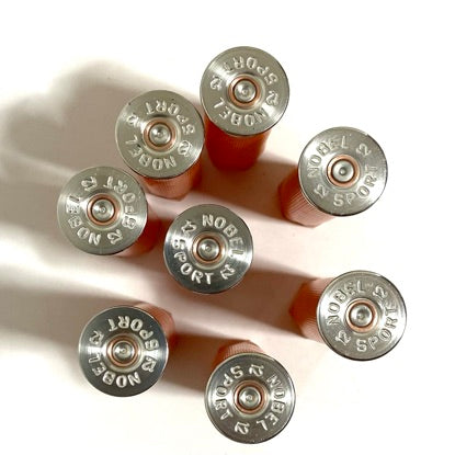 Overhead view of 8 orange 12 gauge shotgun shells showing silver Nobel Sport headstamps arranged in a circle