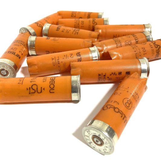 A pile of spent orange 12 gauge Nobel Sport shotgun hulls showing silver metal bases.
