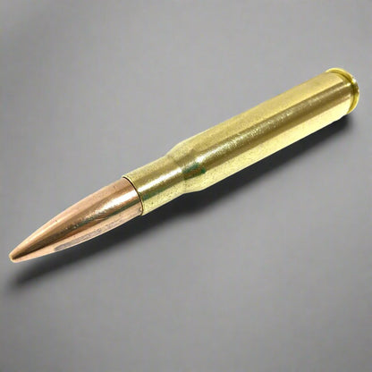 A single 50 caliber weighted paperweight with a polished brass casing and copper bullet lying diagonally against a grey background.
