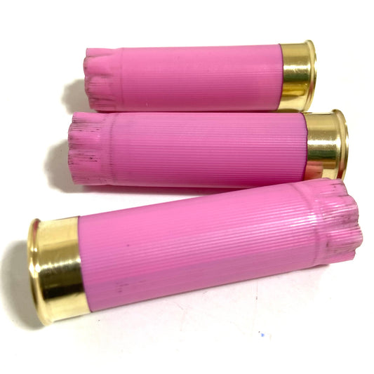 Three empty pink shotgun shells lie diagonally, showing their crimped open ends and gold brass bases.
