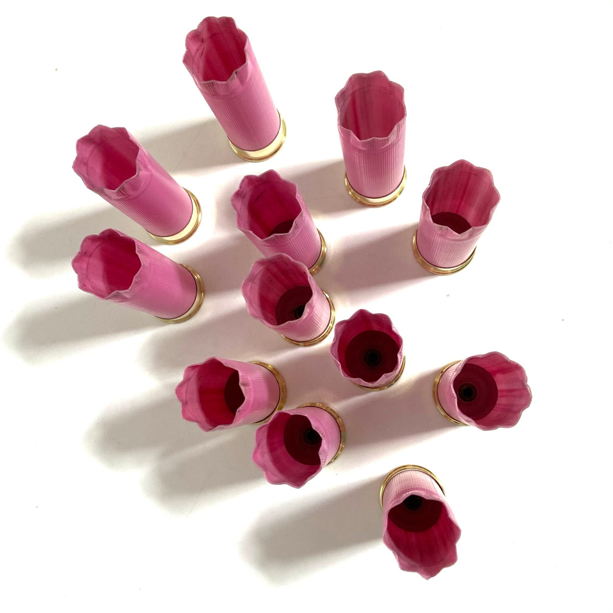 Twelve empty pink shotgun shells viewed from above, standing at varied heights with dark open mouths.