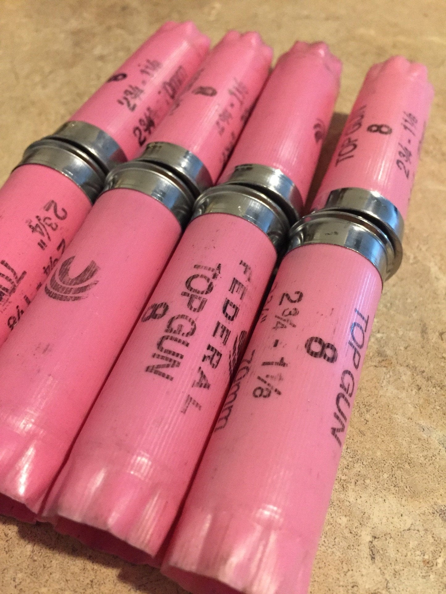 Closeup of four pink Federal Top Gun 12 gauge shotgun shells lying side by side, showing crimped tops and printed markings