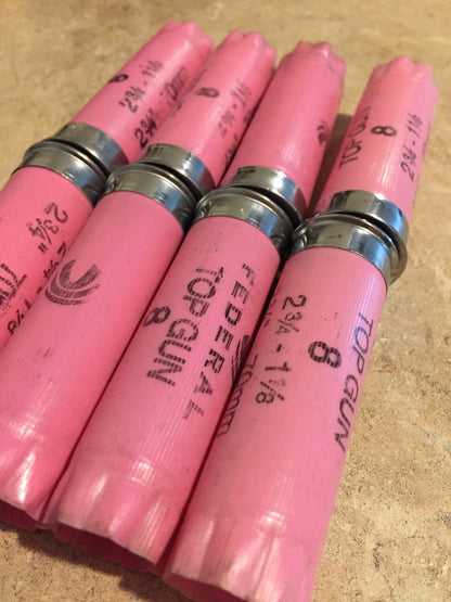 Closeup of four pink Federal Top Gun 12 gauge shotgun shells lying side by side, showing crimped tops and printed markings