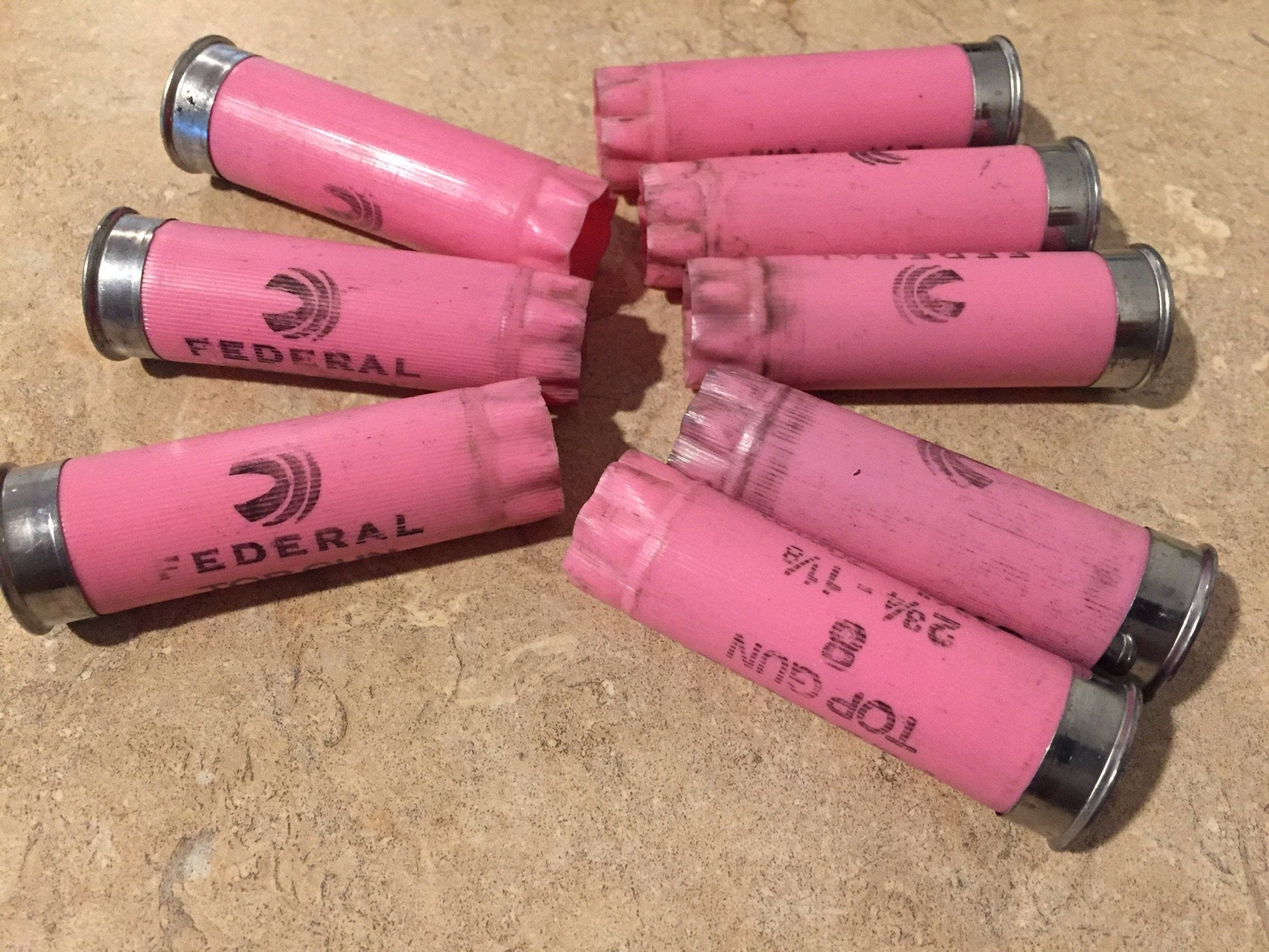 Eight pink Federal Top Gun 12 gauge shotgun shells fanned out, one hull split open showing the red interior