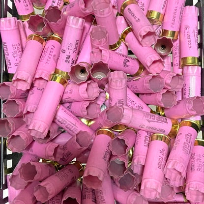 A large pile of pink 12GA Federal Top Gun empty hulls with gold bottoms, packed together in a bin.