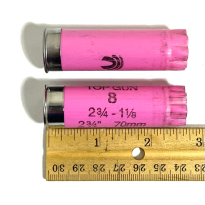 Two pink Federal Top Gun 12 gauge empty shotgun shells laid next to a wooden ruler showing a length of about 2.75 inches