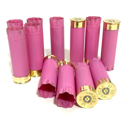 A group of used pink shotgun casings stands and lies in mixed orientations, with two headstamps facing the camera.