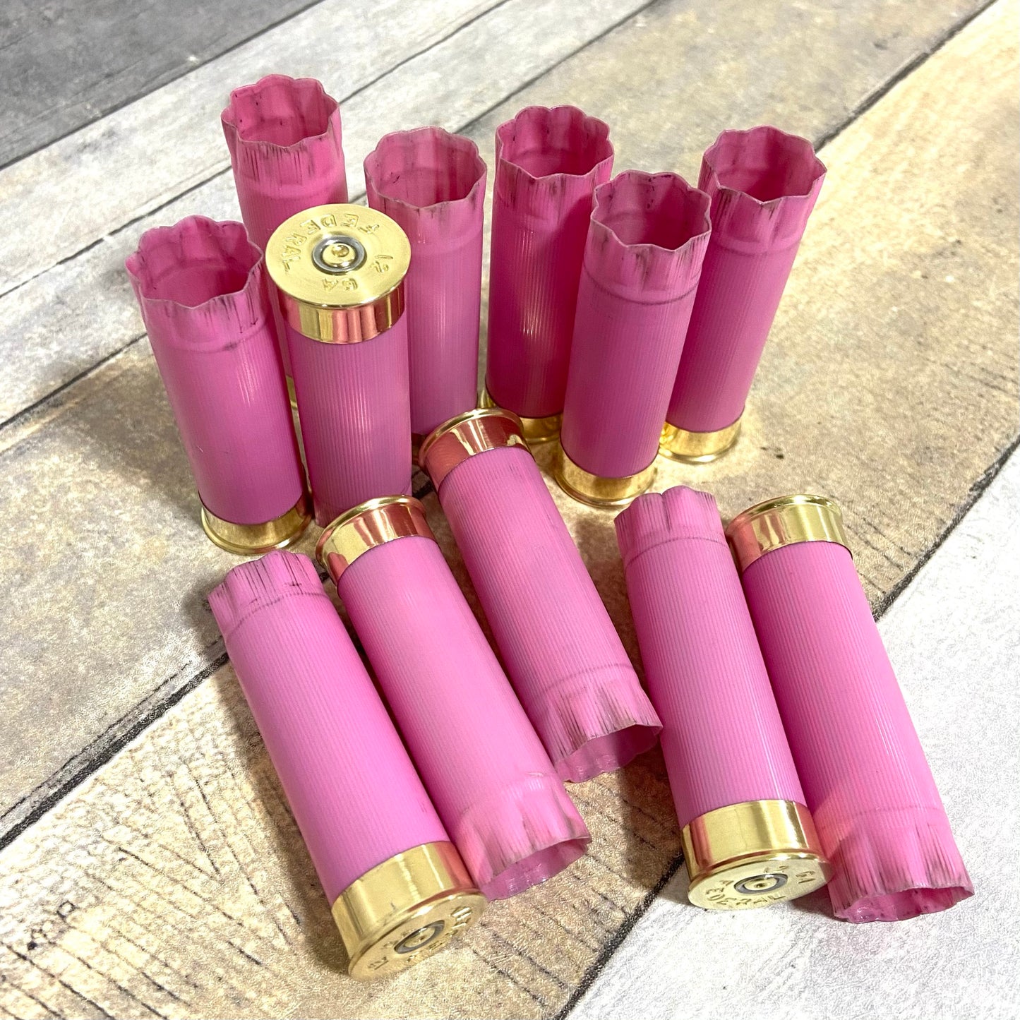 A cluster of used pink shotgun casings stands and rests on a wood plank surface, with one headstamp facing forward.