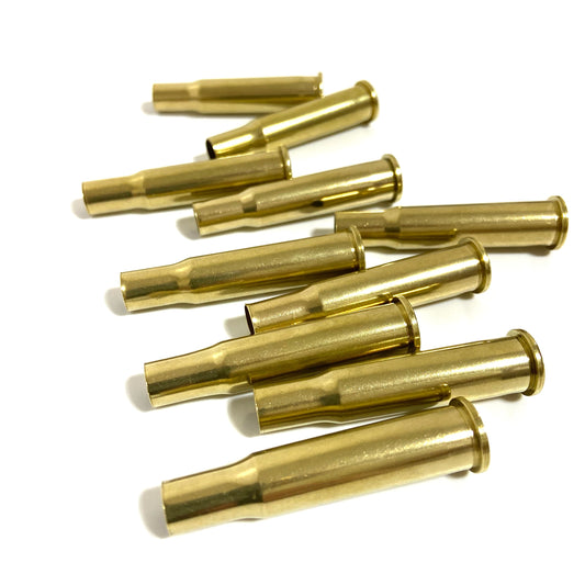 Scattered group of polished 30-30 Winchester brass casings lying flat on white surface, bright yellow-gold shine.

