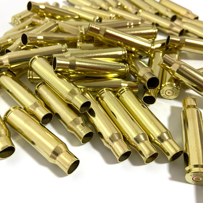 A dense pile of polished gold 308 WIN brass shells on a white background, highlighting open case mouths