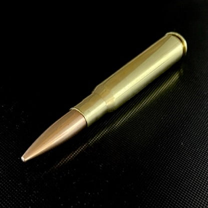 A polished 50 BMG paperweight lying diagonally on a dark textured mesh surface.