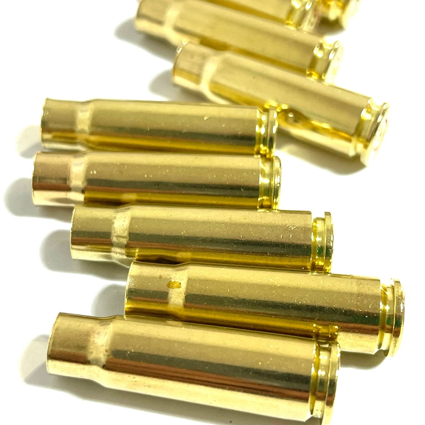 Close-up side view of scattered polished gold-tone 7.62x39 AK-47 brass casings lying flat on a white background.
