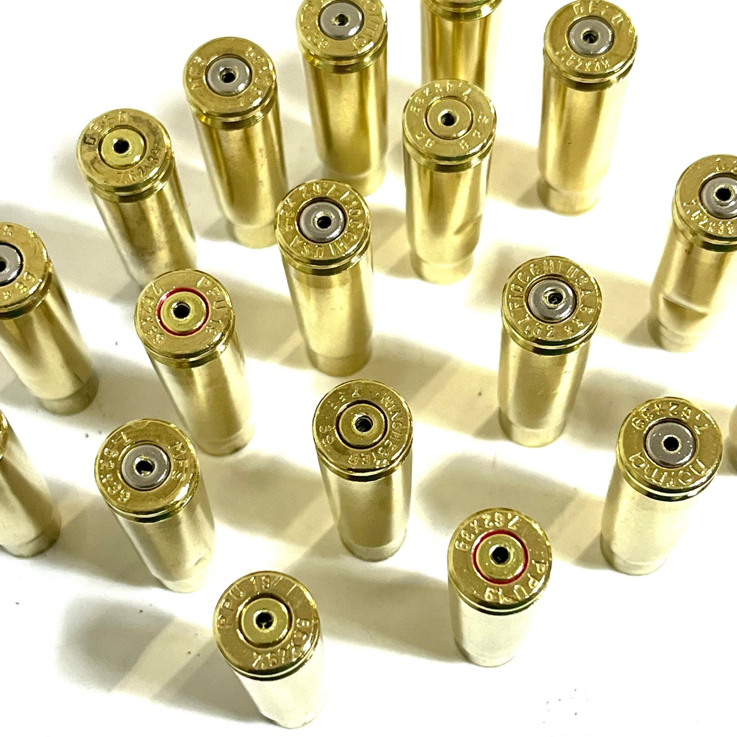 Many spent brass shells standing in a grid, headstamps facing up, casting shadows in soft sunlight.