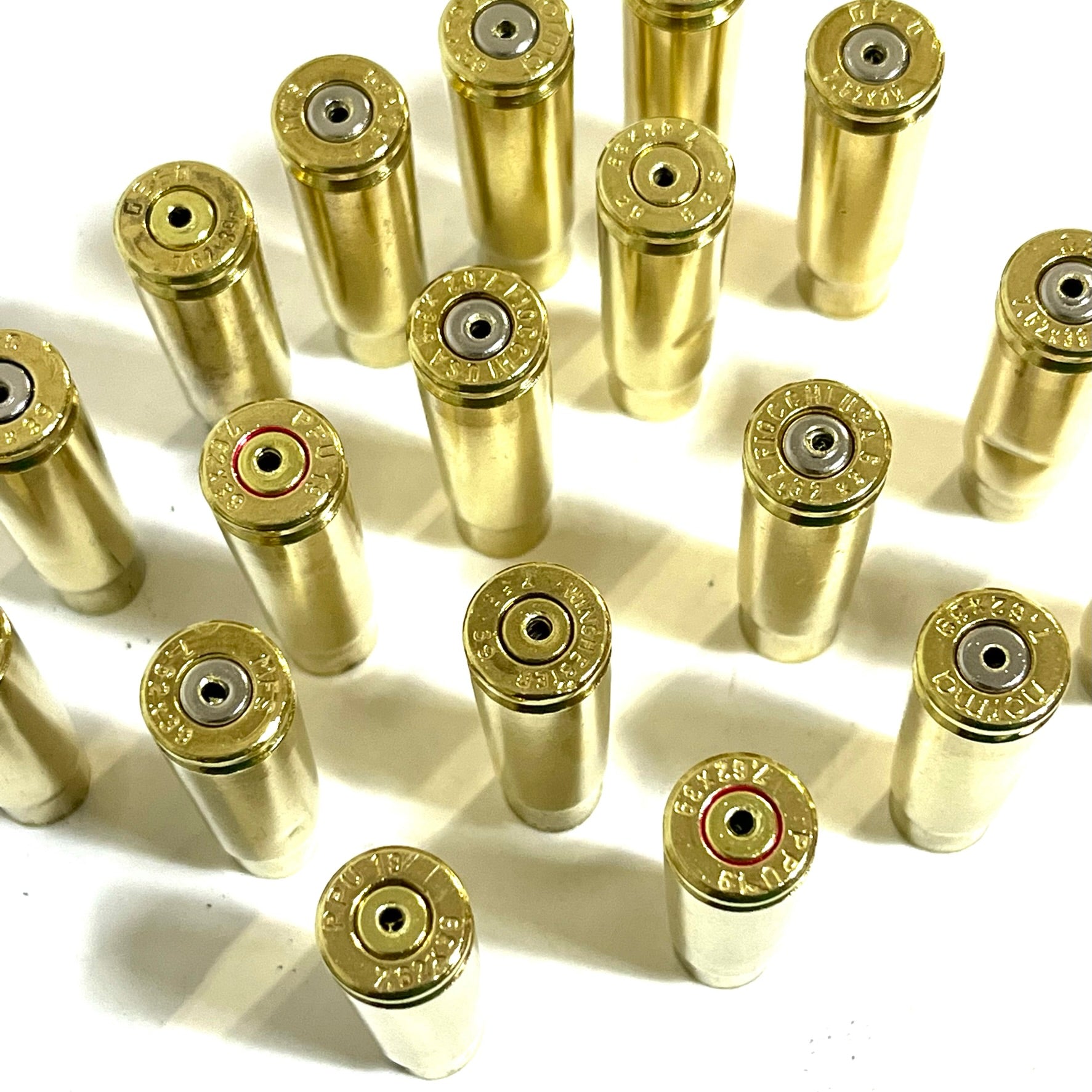 Many spent brass shells standing in a grid, headstamps facing up, casting shadows in soft sunlight.