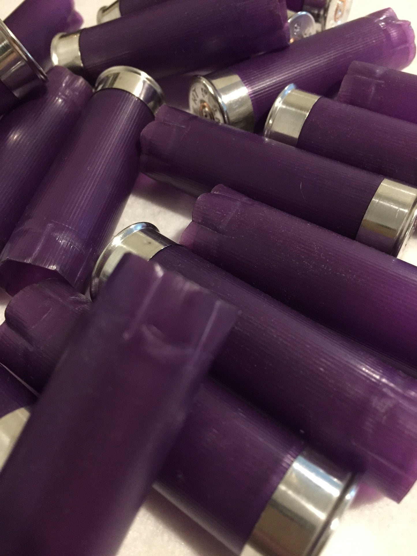 Overhead close-up of purple shotgun shell hulls piled together, silver bases and crimped purple tops overlapping