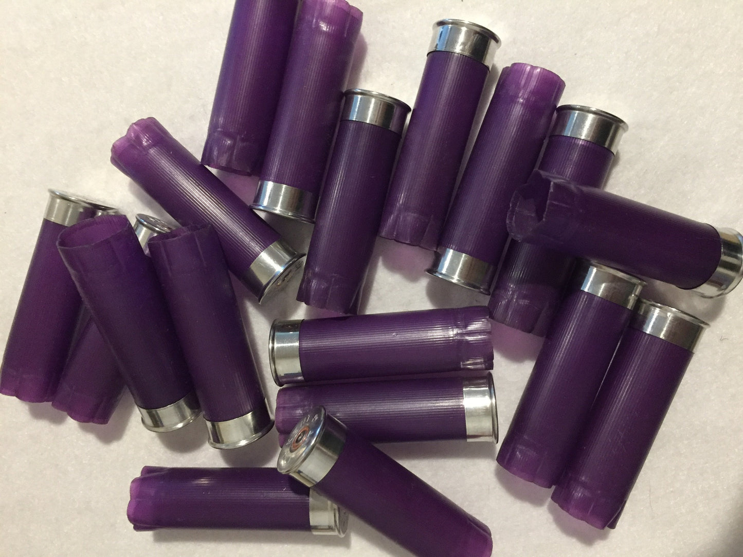 18 purple shotgun shell hulls scattered in a pile on white surface, silver bases and crimped ends visible