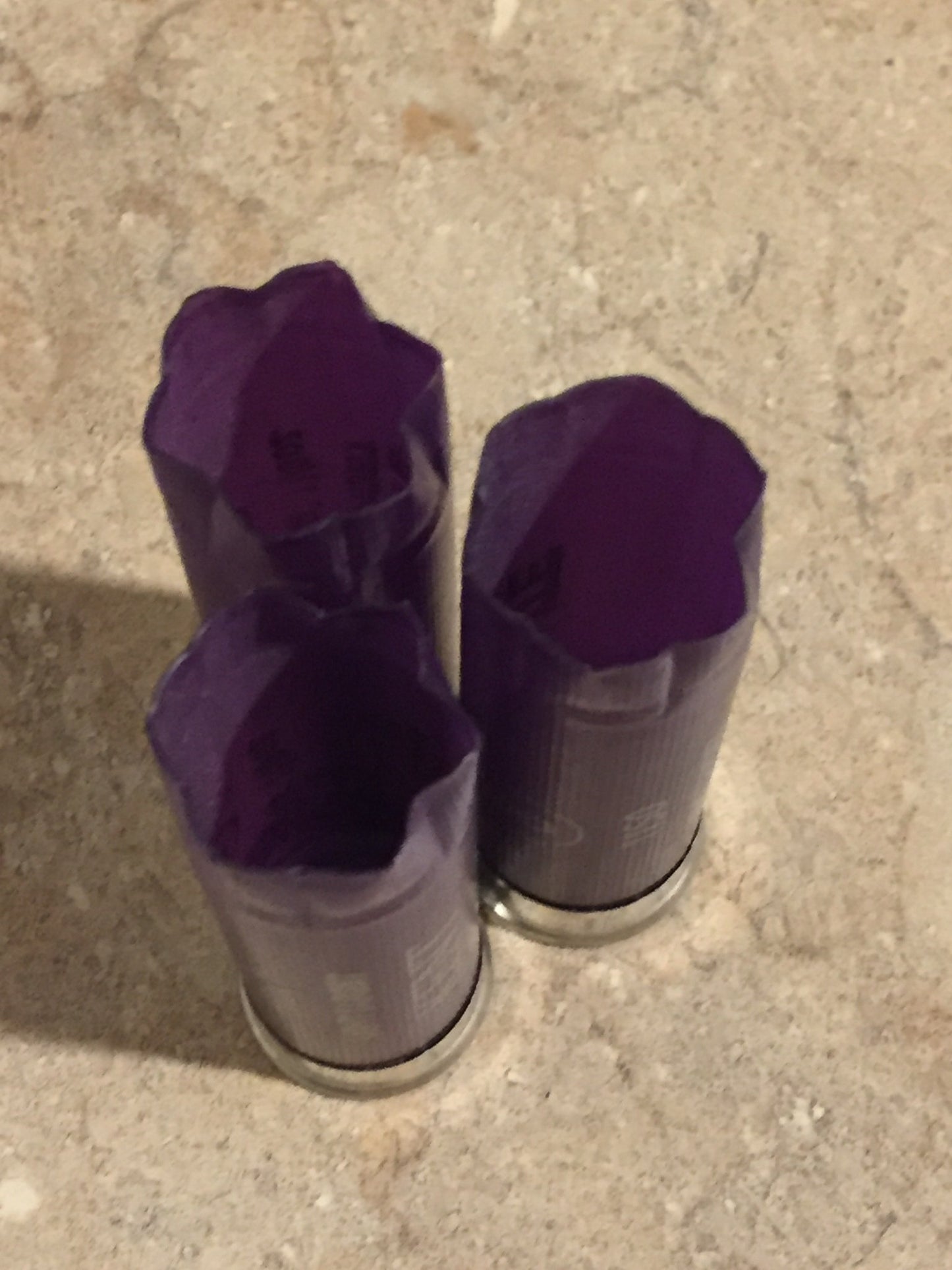 Three purple 12 gauge shotgun shells standing upright with open, star-crimped mouths on a granite countertop