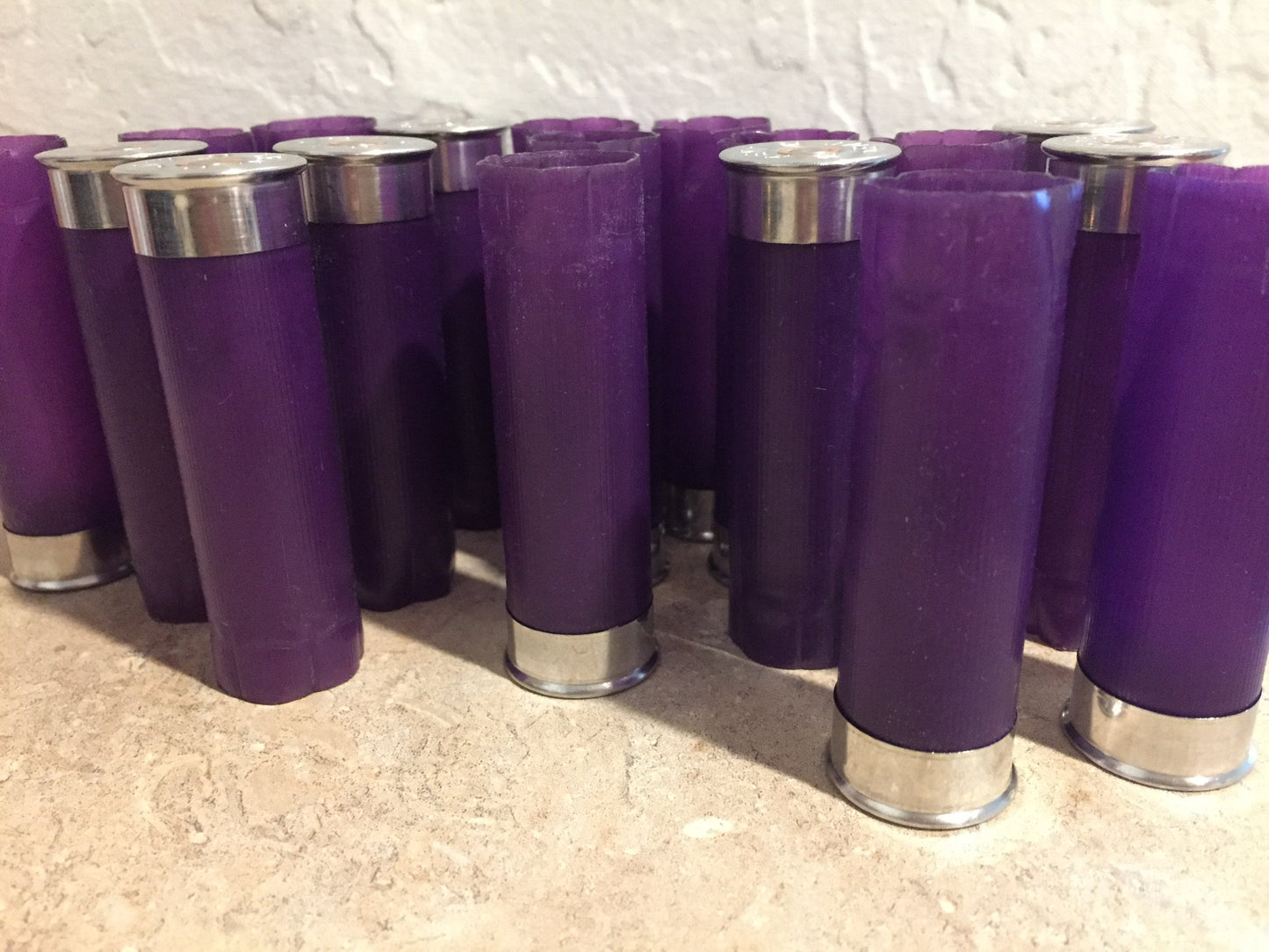 Group of purple shotgun shell hulls standing against white textured wall, mix of silver bases and crimped tops