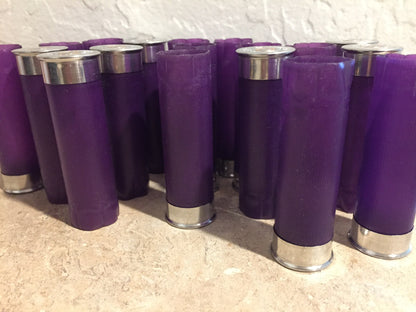 Group of purple shotgun shell hulls standing against white textured wall, mix of silver bases and crimped tops