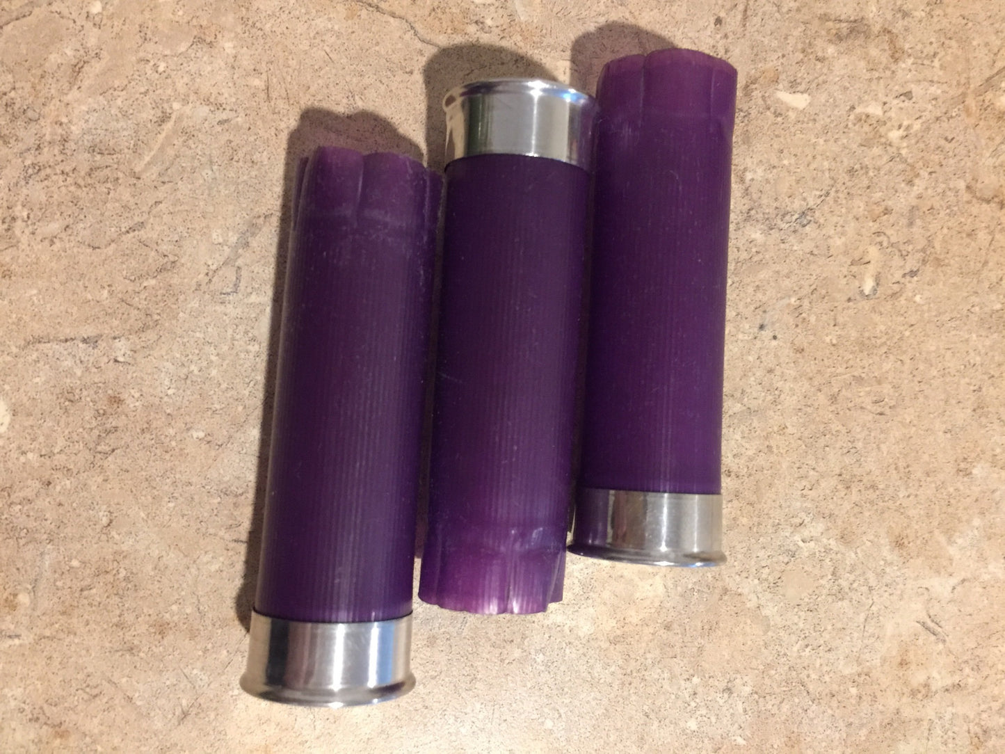 Three purple shotgun shell hulls lying on tile, one showing silver base, two showing crimped purple tops
