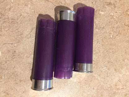 Three purple shotgun shell hulls lying on tile, one showing silver base, two showing crimped purple tops