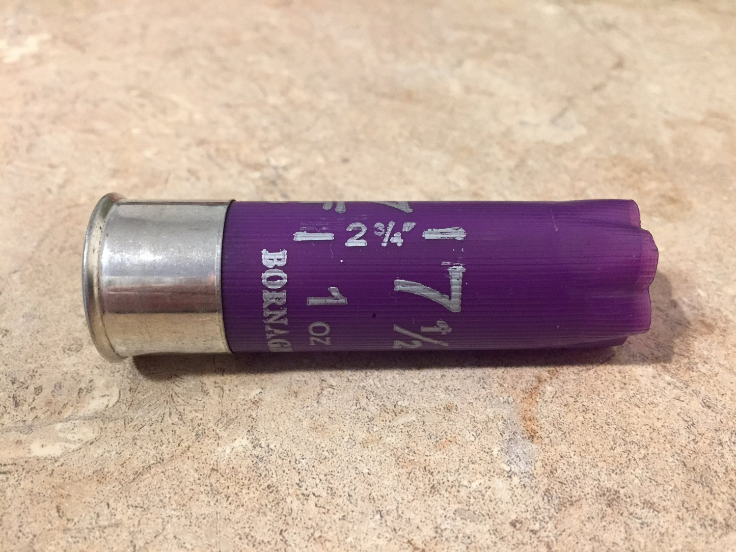 Single purple Bornaghi 12 gauge shotgun shell lying on a stone surface showing silver head and printed text