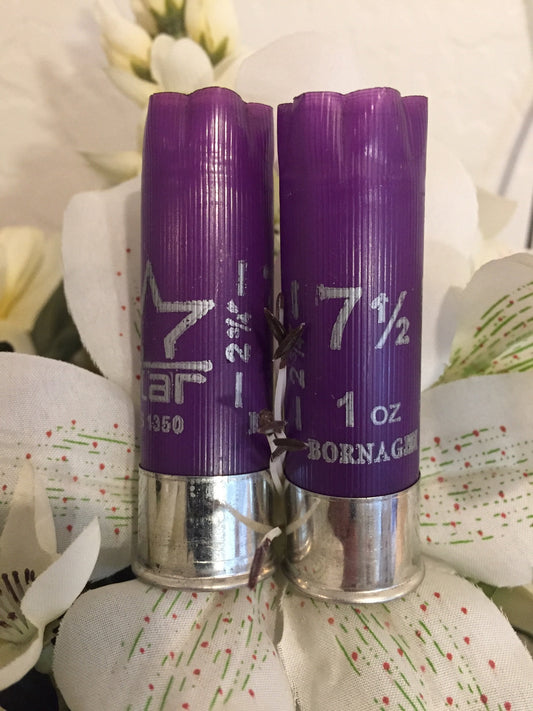 Two purple Bornaghi 12 gauge shotgun shells with silver heads standing among white flowers