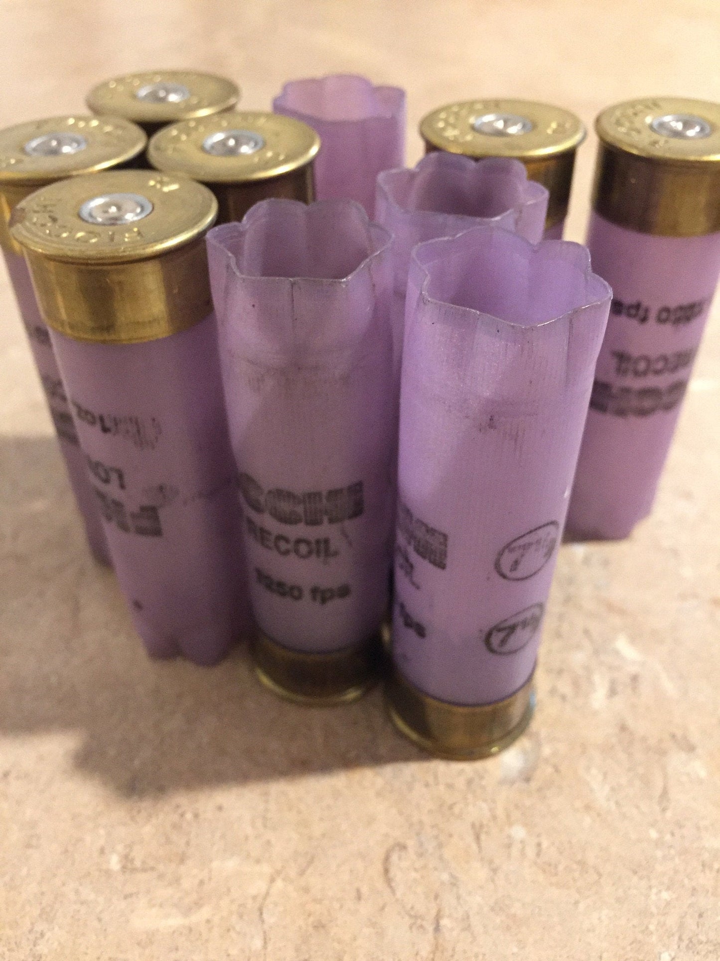 Group of purple Fiocchi Low Recoil 12 gauge shotgun shells, some with crimped star-fold tops and some with brass base caps, on a tile surface